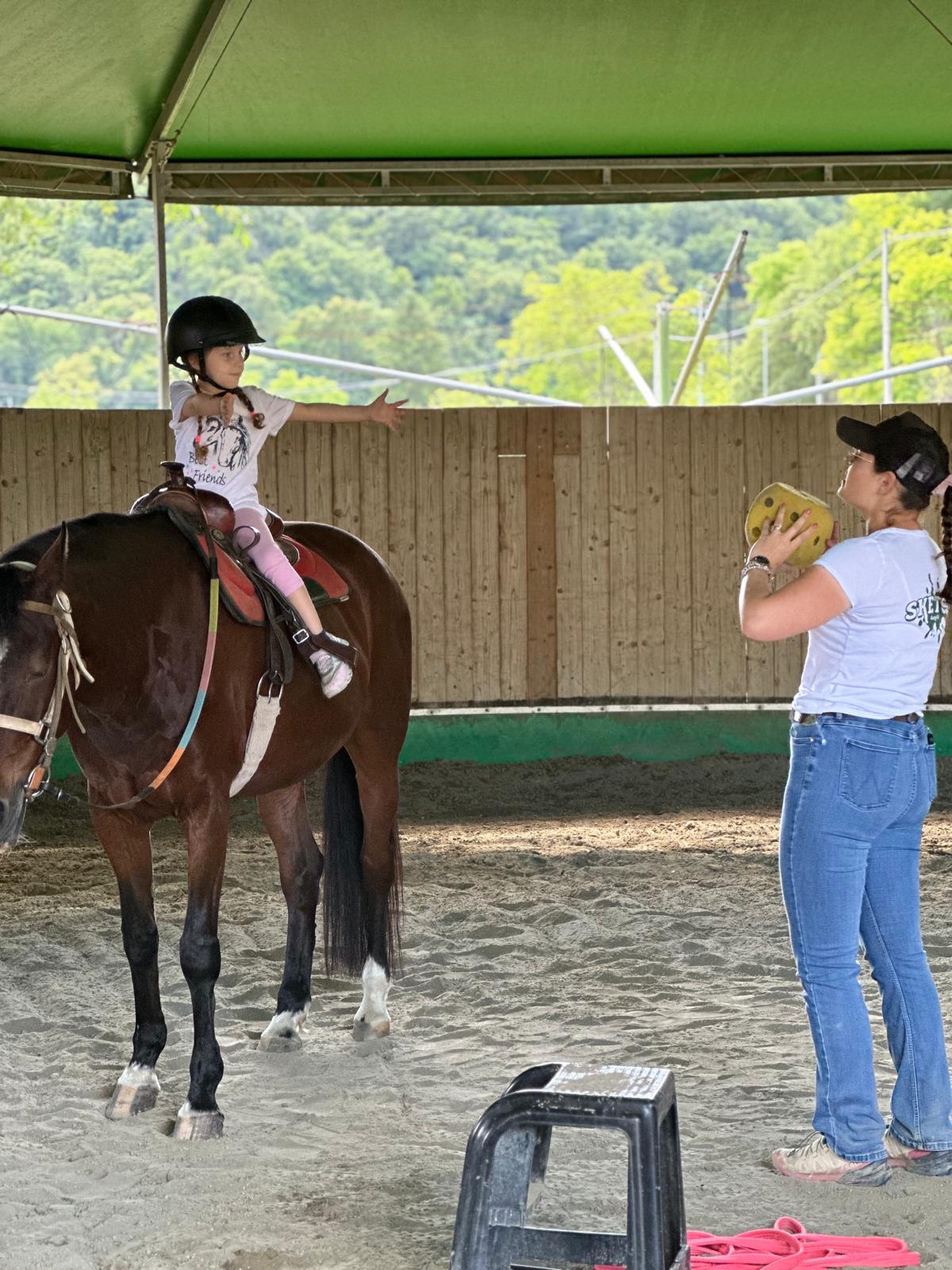 Child riding a horse at a baby farm, guided by an instructor. Equestrian lesson.